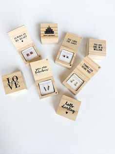 small wooden boxes with different types of earrings in them on a white surface, including one that says love and the other saying i love