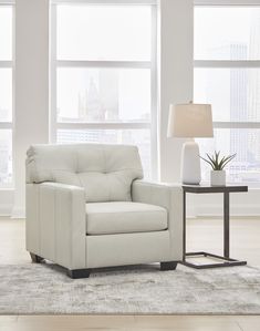 a white chair sitting in front of two windows next to a table with a plant on it