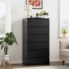 a black dresser in a living room next to a white chair and potted plant