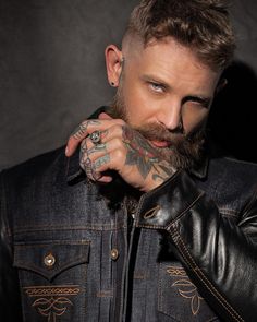 a man with tattoos and piercings on his face wearing a leather jacket, looking at the camera