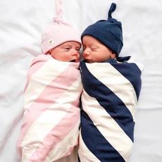 two baby babies wrapped in blankets and sleeping on top of each other, both wearing hats