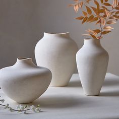 three white vases sitting on top of a table