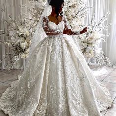 a woman in a wedding dress standing next to a white flowered arch with her hands on her hips