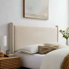 a bed with white linens and pillows in a small room next to a painting on the wall