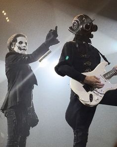 two men in gas masks playing guitars on stage with one man wearing a mask and the other holding a guitar