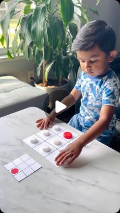 a little boy sitting at a table playing with some sort of board game on it