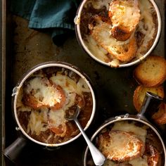 three pots filled with food sitting on top of a baking pan next to bread and utensils