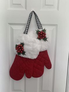 a red mitt hanging on a door decorated with holly berries and white fluffy gloves