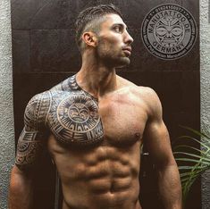 a shirtless man with tattoos on his arm and chest standing in front of a wall