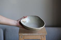 a hand holding a bowl on top of a wooden table next to a gray couch