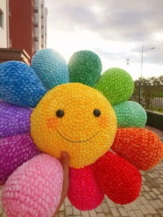 a person holding up a colorful flower made out of knitted balls with a smiley face on it