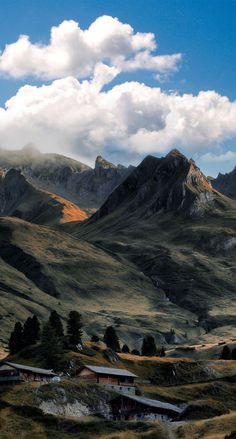 the mountains are covered with green grass and clouds in the distance is a small cabin