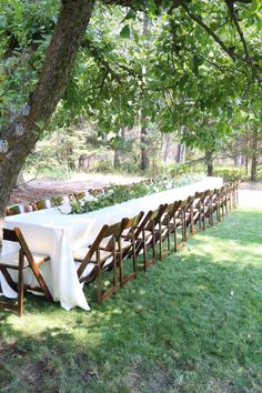 a long table is set up under the shade of a tree