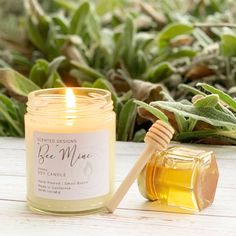 a jar of honey next to a candle on a table with green leaves in the background