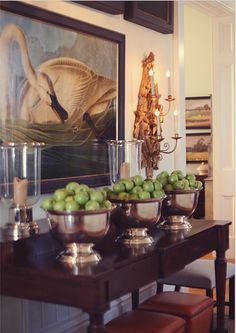 a table topped with bowls filled with green apples next to a wall mounted swan painting