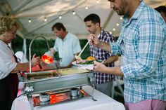 a man is serving food to people at an outdoor event with lights on the ceiling