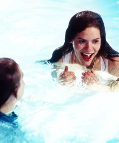 two girls are in the water playing with each other and smiling at each other while one girl is holding her hand out