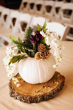 a white pumpkin decorated with greenery and pine cones on a wooden slice at a wedding reception