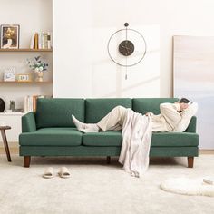 a man laying on top of a green couch in a living room next to a clock