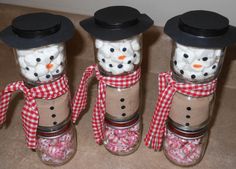 three snowman jars filled with marshmallows and candies in black hats