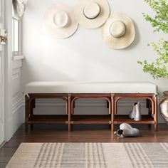 three hats are hanging on the wall above a bench and two vases with flowers