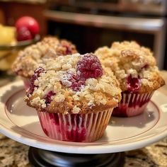 three muffins on a plate with crumbs and fruit in the background