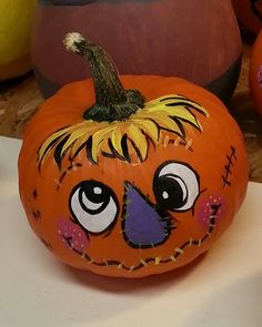 an orange pumpkin with eyes painted on it sitting on a table next to other pumpkins