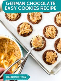 german chocolate cookies with orange icing on a baking sheet and a hand holding a spoon