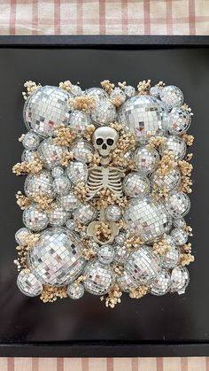 a skeleton surrounded by disco balls in a black frame on a checkered tablecloth