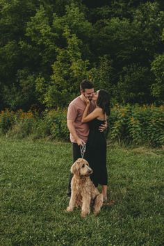 a man and woman standing in the grass with their dog