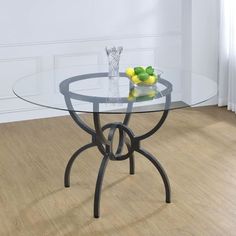 a glass table with some lemons on it in front of a white wall and wooden floor