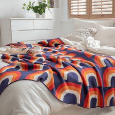 a bed covered in a colorful blanket next to pillows and blankets on top of it