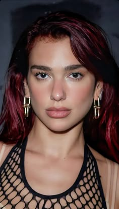 a woman with red hair wearing gold hoop earrings and a black top is looking at the camera