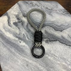 a black and silver keychain on a marble surface with a metal ring hanging from it's end