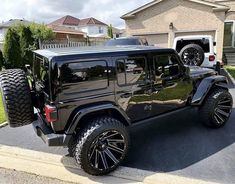 a black jeep parked in front of a house with two large tires on it's rims