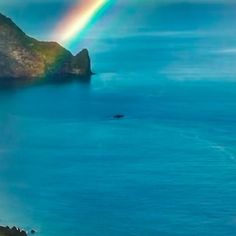 a rainbow shines in the sky over an island and body of water with a boat on it