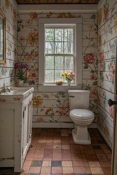 a white toilet sitting in a bathroom next to a sink under a window with flowers on it