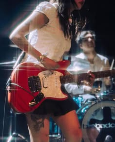 a woman playing guitar while standing next to a man with a band on the other side