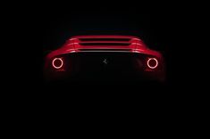 the rear end of a red sports car with its lights turned on in the dark