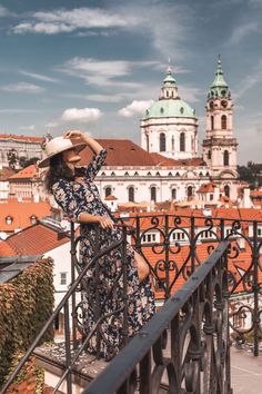 a woman in a dress and hat standing on a balcony looking out at the city