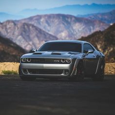 the front end of a gray car parked on top of a dirt field next to mountains