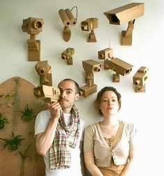 two people standing next to each other in front of a wall with wooden objects on it