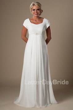 a woman wearing a white dress with short sleeves and a beaded belt is standing in front of a beige background