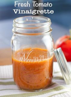 a mason jar filled with orange sauce next to a knife and tomato on a table