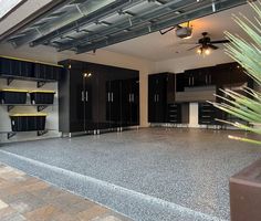 an empty garage with black cabinets and plants in the center, surrounded by concrete flooring