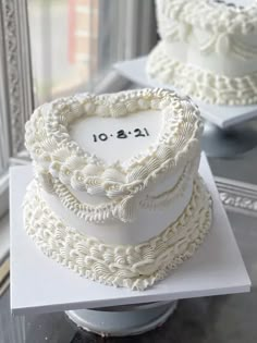 two tiered wedding cakes with white frosting on display in front of a window