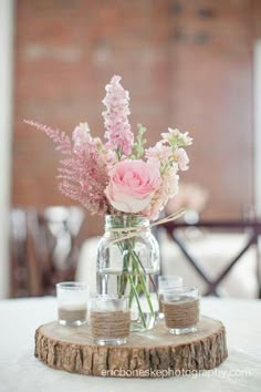 a vase filled with pink flowers sitting on top of a wooden table next to two glasses