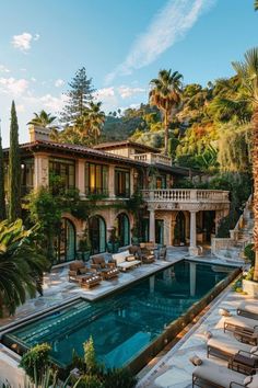 an outdoor pool surrounded by palm trees and lawn furniture in front of a large house