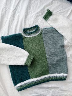 a green and white sweater laying on top of a bed