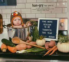 a baby is sitting in a pot with vegetables on the stove top and next to it is a sign that says, one more reason to be thank you this year